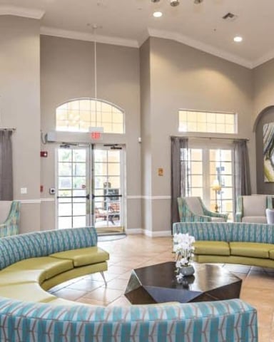 Spacious lobby with curved blue and green seating, arched doorways, and glass doors opening to exterior